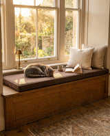 Cat sleeping on a brown boucle cushion on a wooden window seat
