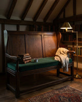 Green velvet cushion on a dark wooden settle in a library