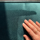 Hand touching the surface of a dark teal velvet cushion