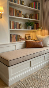 Beige cushion with brown piping on a reading nook bench below bookshelves