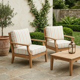 Striped square seat and back cushions on two teak lounge chairs in a courtyard