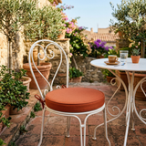 Terracotta round cushion on a white iron bistro chair on a patio