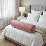 Dusty pink bolster pillow across a bed with white bedding