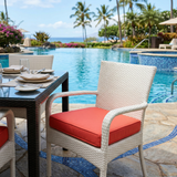 Coral red square seat cushion on a white wicker dining chair by a pool