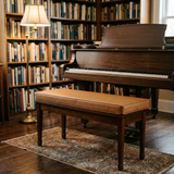 Tan cushion on a piano bench in front of a grand piano in a library