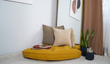 Mustard quarter-round tufted floor cushion with pillows in a room corner