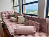 Pink tufted seat and back cushions with bolsters by a sea-view window