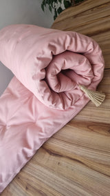 Rolled pink quilted topper with a tassel on a wooden surface