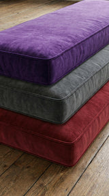 Stacked velvet cushions in purple, gray and red on a wood floor