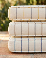 Three stacked striped outdoor cushions on a terracotta patio