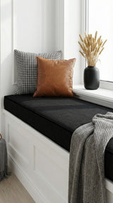 Black cushion on a white window seat with leather and houndstooth pillows