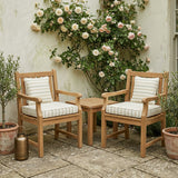 Striped cushions on two teak armchairs by a rose-covered wall
