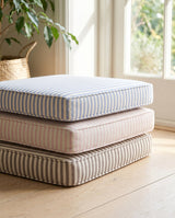 Stacked striped cushions in blue, blush and taupe on a wood floor