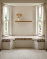 Patterned cushions on a white bay window seat with a floating shelf