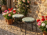 Green round seat pads on two metal bistro chairs among flowers