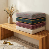 Stack of point weave cushions in gray, green, plum and cream on a bench