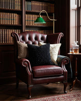 Black textured pillow on an oxblood leather armchair in a library
