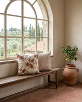 Rust blossom and beige pillows on a bench below an arched window