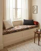 Rust paisley cushion on a cream window seat with a round bolster