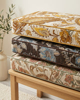 Stacked paisley cushions in gold, navy and rose on a wooden bench