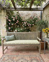 Sage patterned cushion on a teak bench in a rose courtyard