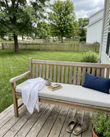 Light gray cushion on a teak bench on a backyard deck