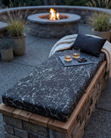 Black marble-print cushion on a stone bench by a fire pit