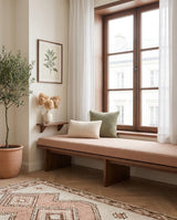 Blush boucle cushion on a wooden bench below a window