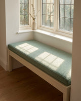 Sage boucle cushion on a white bench by a leaded window