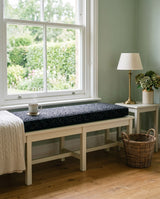 Black speckled cushion on a white bench by a garden window